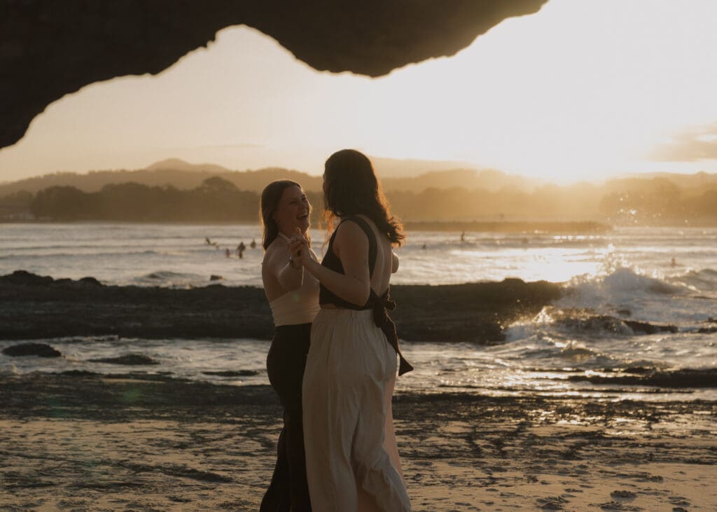 A couple dancing on the sand at Currumbin Beach with surfers in the background